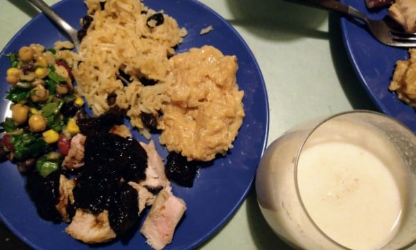 A blue plate with food on it; rice, chicken, beans, corn, next to a glass of white liquid.